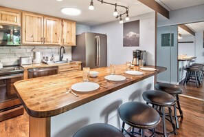 A modern kitchen with wooden cabinets, a stainless steel refrigerator, a built-in island with bar stools, and a coffee machine. - Ski In - Ski Out. Perfect Location. Hot Tub. Pool. (Breckenridge)