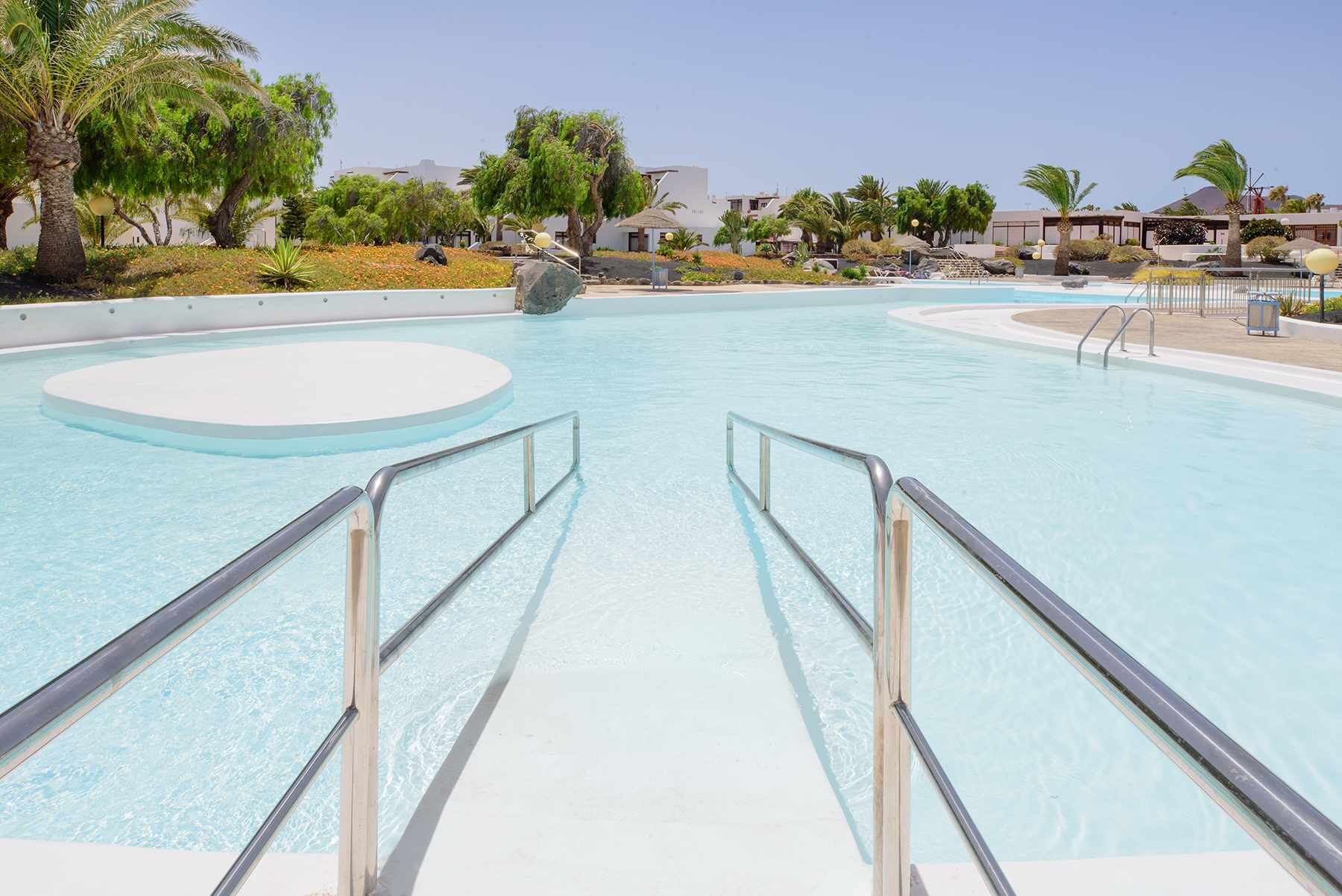 A large, clear swimming pool with a central island and a circular deck area.