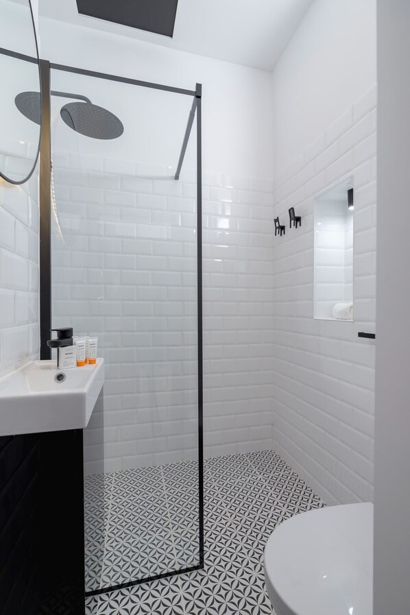 A modern bathroom with white subway tiles, a black-framed glass shower, and a white sink with toiletries.