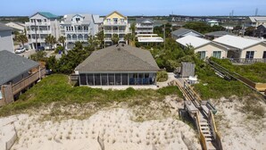 A beachfront property with multiple-story buildings, a covered outdoor seating area, and a wooden boardwalk leading to the beach. - Wave To Cool: 4-bedroom oceanfront cottage in Surf City, NC. (Surf City)