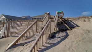 A wooden staircase leading to a private property, with a clear sky and houses in the background. - Wave To Cool: 4-bedroom oceanfront cottage in Surf City, NC. (Surf City)
