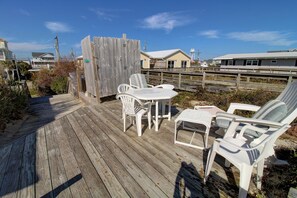 En träveranda med ett bord och stolar, med utsikt över en strand och några hus.
