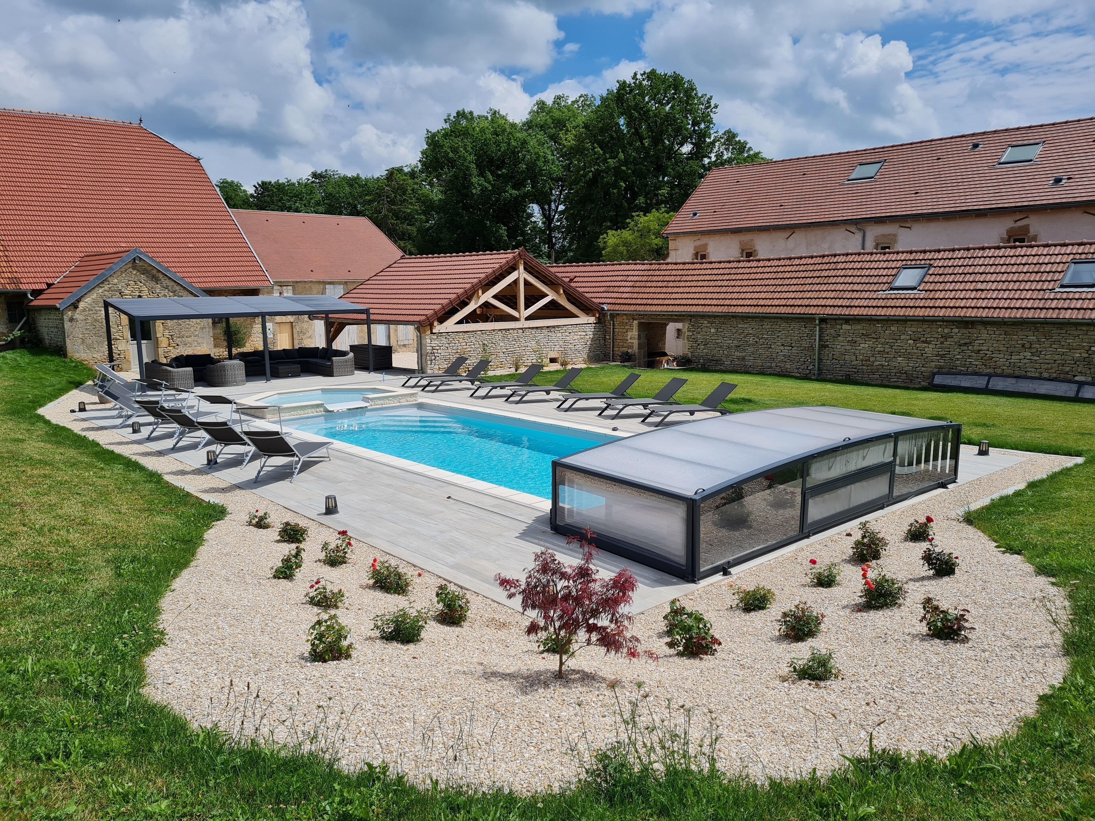 Une piscine dotée de chaises longues et d’un espace de repos couvert, entourée d’un jardin aménagé avec du gravier et de petites plantes.