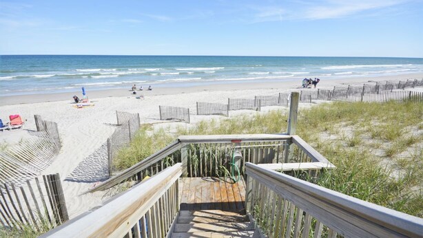Una escalera de madera que da a una playa con un sendero de arena y una valla de madera.