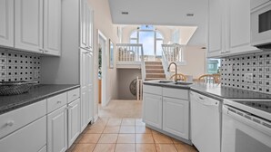 Una cocina moderna con armarios blancos, encimera negra y vista a un balcón con escaleras.