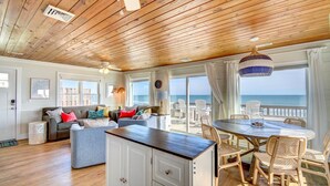 A spacious living area with a wooden ceiling, a large dining table, and a view of the ocean. - Oceanfront, 3-bedroom Whale Song in Surf City - perfect for 7 guests. (Surf City)