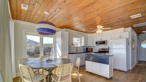 A kitchen with white cabinets, a microwave, and a refrigerator. There is a dining table with wicker chairs and a hanging light fixture. - Oceanfront, 3-bedroom Whale Song in Surf City - perfect for 7 guests. (Surf City)