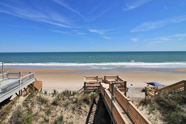 A beach with wooden walkways leading to the shore, a clear blue sky, and calm ocean waves.