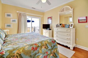 A bedroom with a bed, a dresser, a television, and a balcony door.