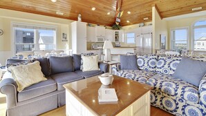 A spacious living area with a wooden ceiling, a large sofa set, a coffee table, and a kitchen in the background. - C-Breeze: Oceanfront 4BR home in Surf City, NC, sleeps 13 comfortably. (Surf City)