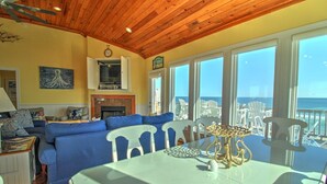 A living room with a blue sofa, a fireplace, and a view of the ocean through large windows. - C-Breeze: Oceanfront 4BR home in Surf City, NC, sleeps 13 comfortably. (Surf City)