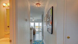 Um corredor com carpete estampado em azul com padrão de estrelas, um ventilador de teto e vista para uma varanda com mobiliário de exterior.