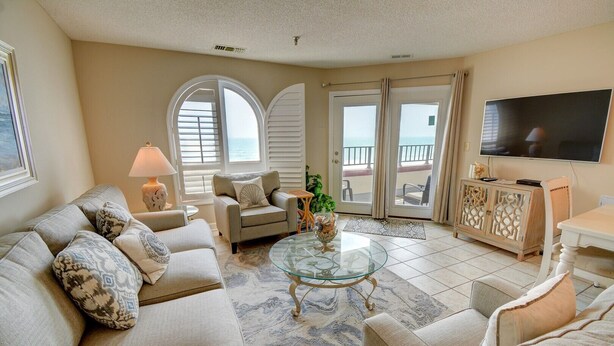 A living room with a sofa, armchairs, a glass coffee table, a TV, and a view of the sea through large windows. - Oceanfront 3BR Villa Capriani 315B in North Topsail Beach, perfect for families! (N Topsail Beach)