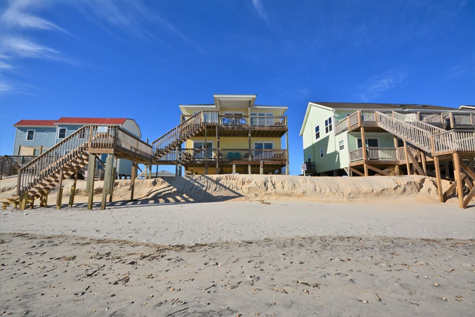 A beachfront property with wooden staircases leading to balconies, a sandy beach, and buildings with multiple stories.