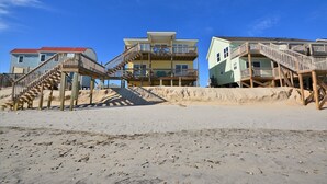 Ein direkt am Strand gelegenes Anwesen mit Holztreppen, die zu Balkonen führen, einem Sandstrand und mehrstöckigen Gebäuden.