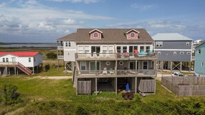Une maison à plusieurs étages située en bord de mer, dotée d’un balcon, d’une terrasse couverte et offrant une vue sur l’océan.