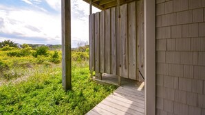 Une terrasse en bois mène à un espace extérieur abrité d’où l’on peut admirer un paysage verdoyant et des bâtiments situés au loin.