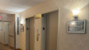 A hotel hallway with patterned carpet, doors numbered 1 and 2, and a wall-mounted light fixture. - Originally built in Chautauqua Institution in 1890, the original St. Elmo Hotel building was torn down and rebuilt as a residential condominium.  It now offers the convenience of an elevator (Chautauqua)