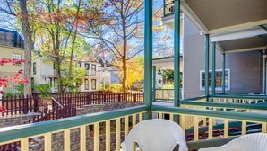 A porch with wicker chairs, a stone wall, and a view of neighboring houses. - Originally built in Chautauqua Institution in 1890, the original St. Elmo Hotel building was torn down and rebuilt as a residential condominium.  It now offers the convenience of an elevator (Chautauqua)