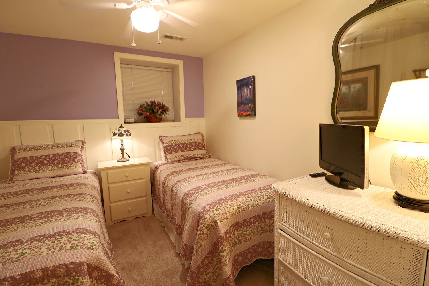 A bedroom with two beds, a nightstand, a dresser, a television, and a window with blinds.
