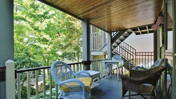 Eine überdachte Veranda mit Korbstühlen, einem Tisch und einer Treppe, die zu einer oberen Ebene führt.