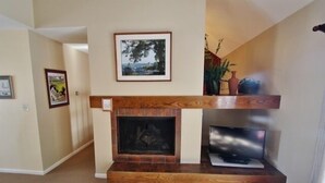 Una sala de estar con chimenea, un televisor sobre un soporte de madera y cuadros en la pared.