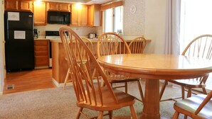 Una cocina compacta con armarios de madera, un refrigerador negro, un microondas y un comedor con una mesa de madera redonda y sillas a juego.