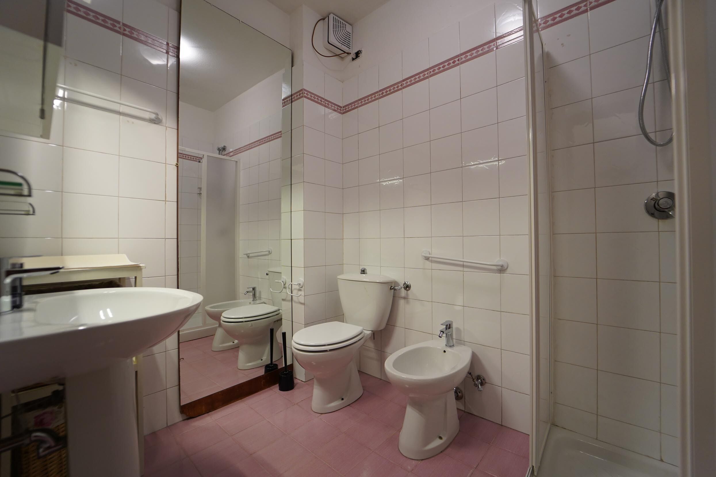 A bathroom with a sink, two toilets, a bidet, and a shower.