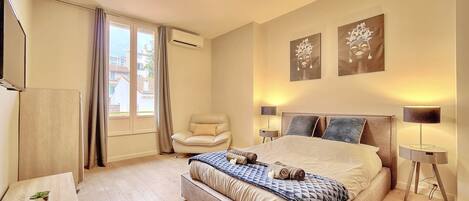 A modern bedroom with a large bed, a chair, a desk, and artwork on the walls.