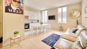 A modern living room with a beige sofa, a dining area with a white table and chairs, a kitchen with white cabinets, and a large window. - Croisette -palais festival-Citycenter -confortable, Croisette - palais festiva l- Citycenter  (Cannes)