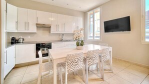 A modern kitchen with white cabinets, a dining table with four chairs, and a flat-screen TV mounted on the wall. - Croisette -palais festival-Citycenter -confortable, Croisette - palais festiva l- Citycenter  (Cannes)