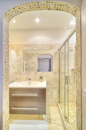 Une salle de bain avec un grand lavabo, un miroir, un espace douche et un mur carrelé.