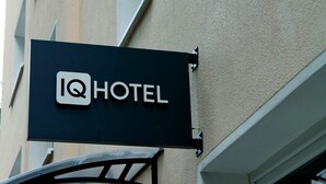 A black sign with a white logo and the word "HOTEL" on a building facade. - IQ Hotel (Hannover)