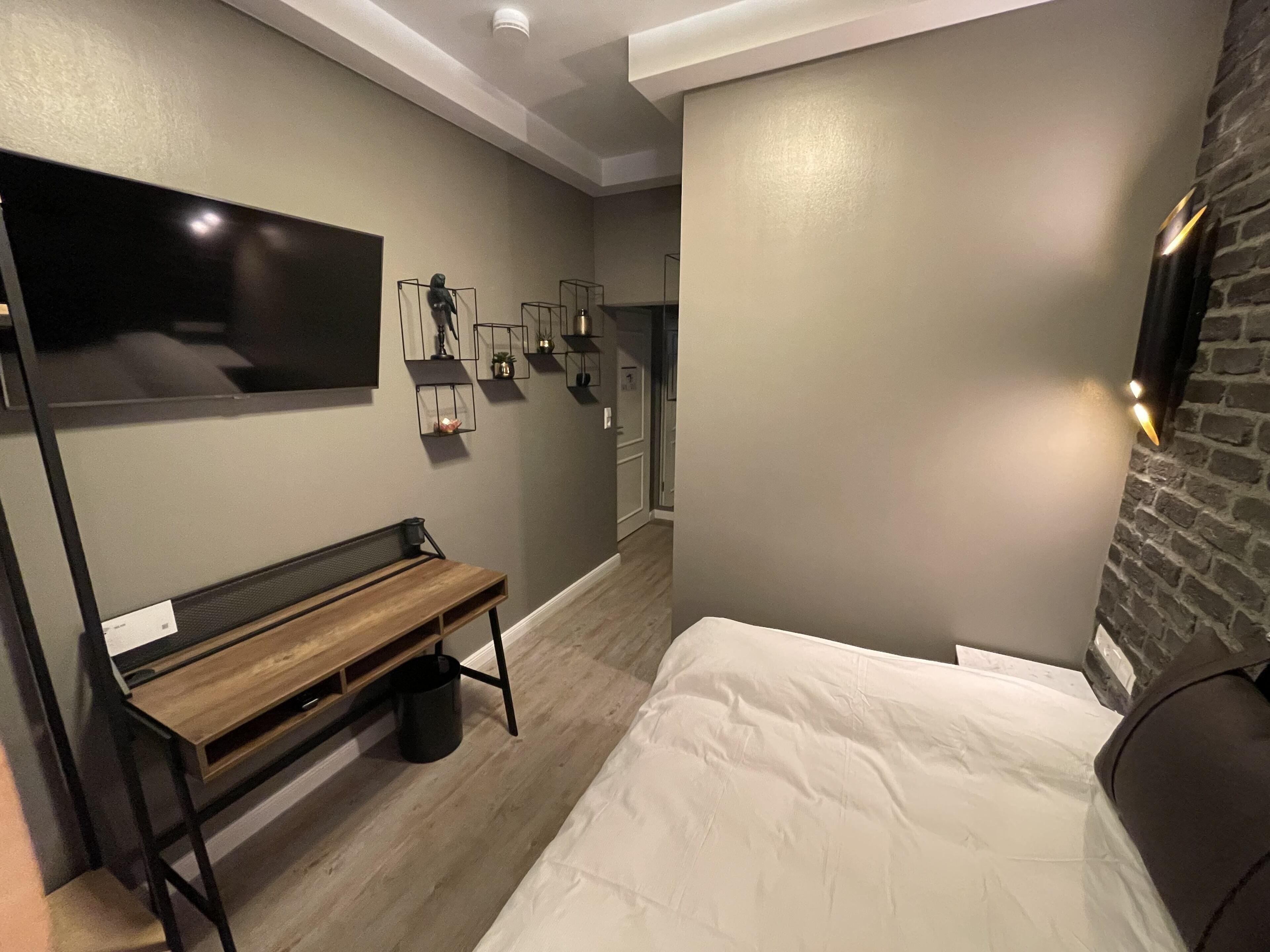 Ein modernes Hotelzimmer mit Bett, Sitzbank, Fernseher und einer Wand aus Ziegelsteinen.