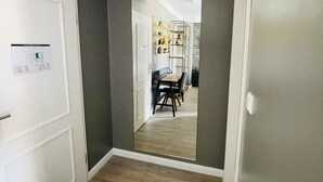 A hallway with a wooden floor, a white door, and a mirror reflecting a dining area with a table and chairs. - IQ Hotel (Hannover)