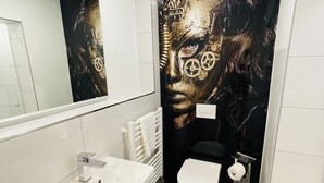 A modern bathroom with a white sink, a toilet, and a large wall mural. - IQ Hotel (Hannover)