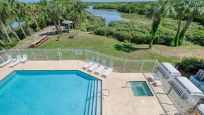 A swimming pool with lounge chairs and a view of a river and palm trees. - Nature's Landing B203 Seasalt in Historic CedarKey (Cedar Key)