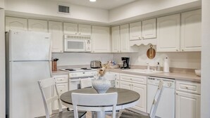 A kitchen with white cabinetry, a refrigerator, a microwave, a stove, and a dishwasher. There is a round dining table with chairs and a vase with dried flowers. - Nature's Landing B203 Seasalt in Historic CedarKey (Cedar Key)