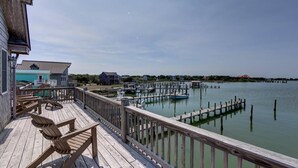 A wooden deck with chairs, a view of a marina with docks and boats, and buildings in the background. - Spencer's Landing - Ocracoke Island (Ocracoke)