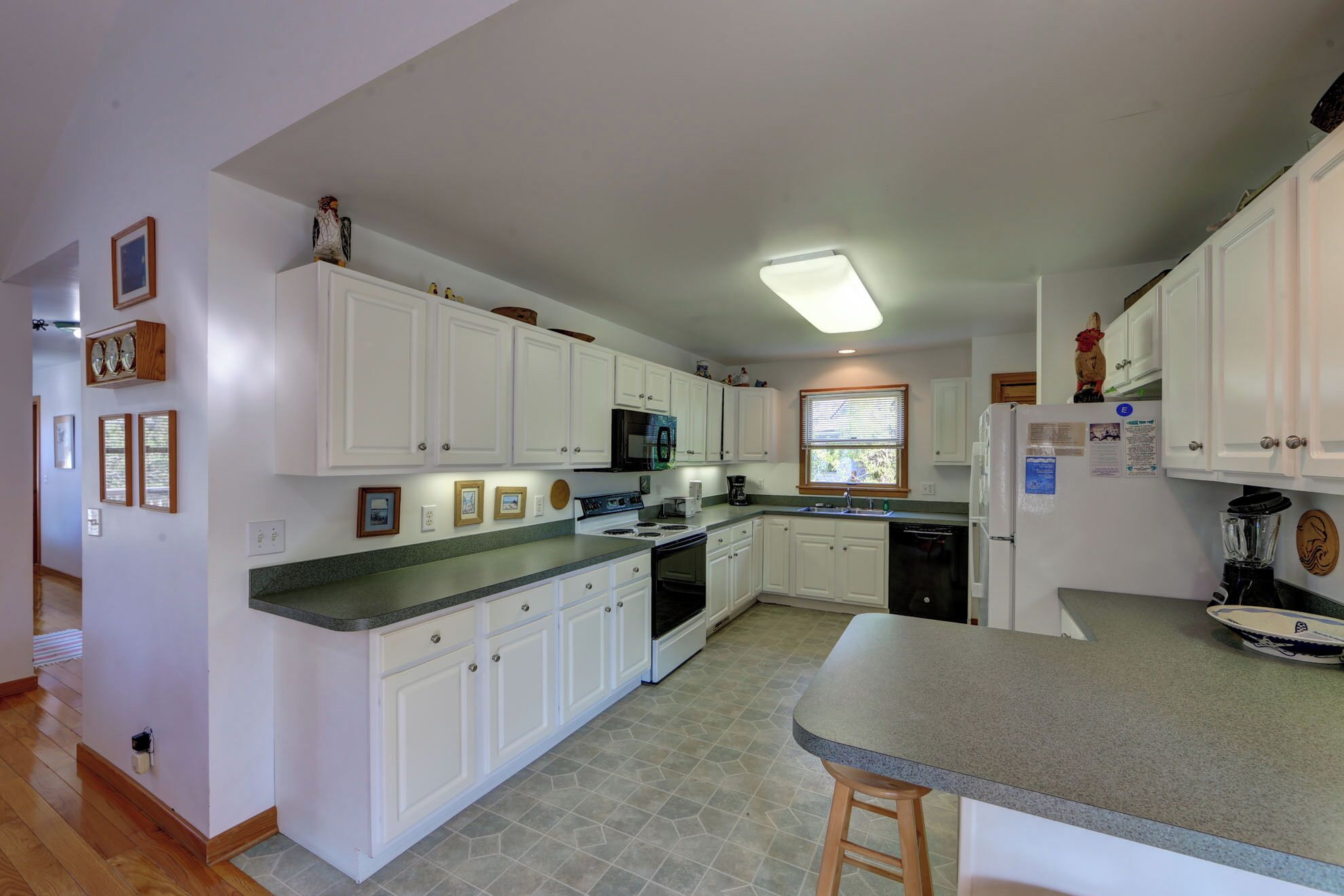 A kitchen with white cabinets, a granite countertop, a built-in oven, a refrigerator, and a window with blinds.