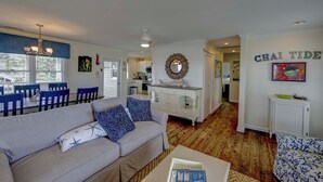 A spacious living area with a sofa, dining table, and chairs, a kitchen in the background, and a wall with 'CHAI TIDE' written on it. - Chai Tide - Ocracoke Island (Ocracoke)