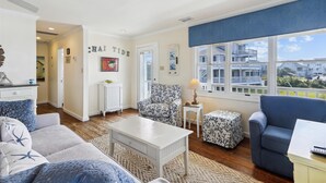 A living room with a view of a coastal building, a white radiator, a patterned armchair, and a blue sofa. - Chai Tide - Ocracoke Island (Ocracoke)