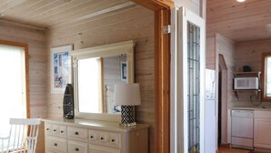 Un interior de madera con un aparador, una mecedora, un espejo, una lámpara y una zona de cocina con microondas y refrigerador.