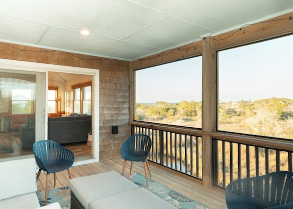 A covered outdoor area with a wooden deck, two blue chairs, a sofa, and a view of a natural landscape.