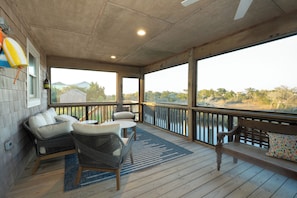 A covered outdoor deck with wicker furniture, a bench, and a view of the landscape.