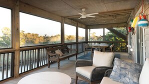 Eine überdachte Veranda mit Holzboden, Deckenventilator, Tisch, Sofa und einer Bank.