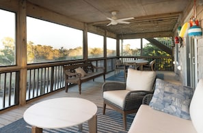 A covered porch with wooden flooring, a ceiling fan, a table, a sofa, and a bench.