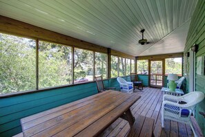 A covered porch with a wooden table and chairs, large windows, and a ceiling fan. - Widgeon's Rest - Ocracoke Island (Ocracoke)
