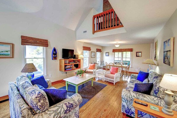A spacious living room with a high ceiling, a wooden staircase, and a television on a wooden stand. - Widgeon's Rest - Ocracoke Island (Ocracoke)