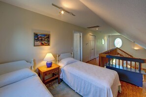 A bedroom with two beds, a nightstand, a lamp, a painting, and a staircase leading to an upper level. - Widgeon's Rest - Ocracoke Island (Ocracoke)